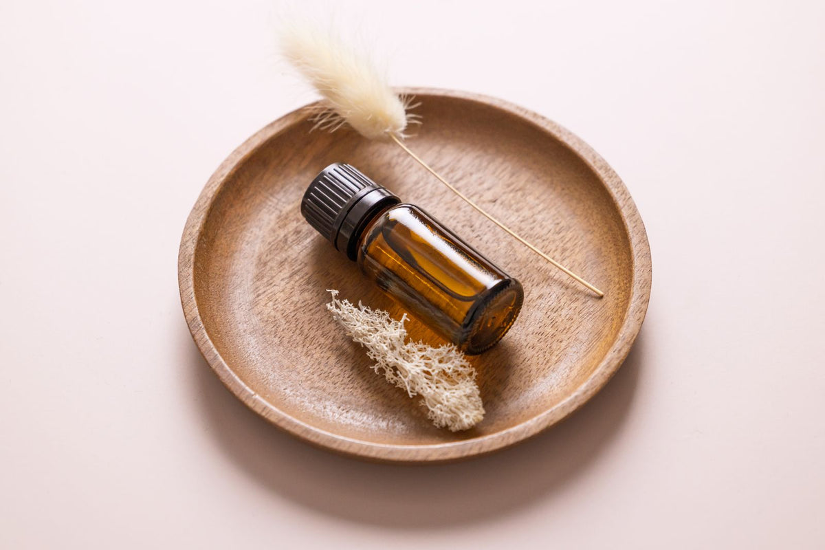 A minimalist still life featuring an essential oil bottle on a wooden plate with decorative elements