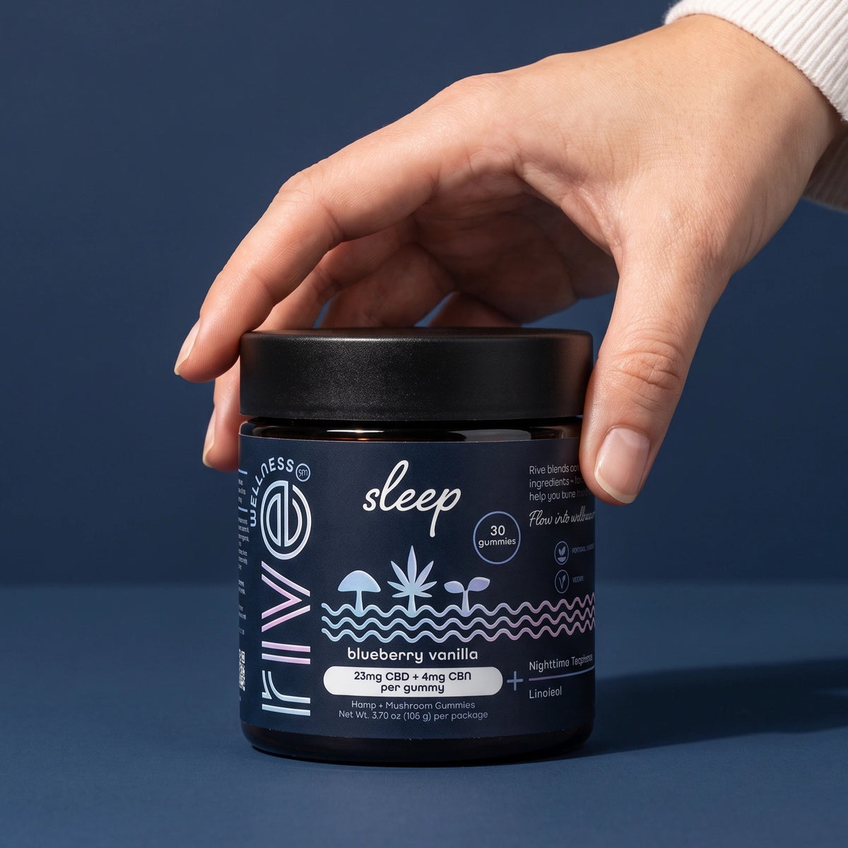A hand resting on the lid of a Rive Sleep blueberry vanilla gummy jar against a navy blue background