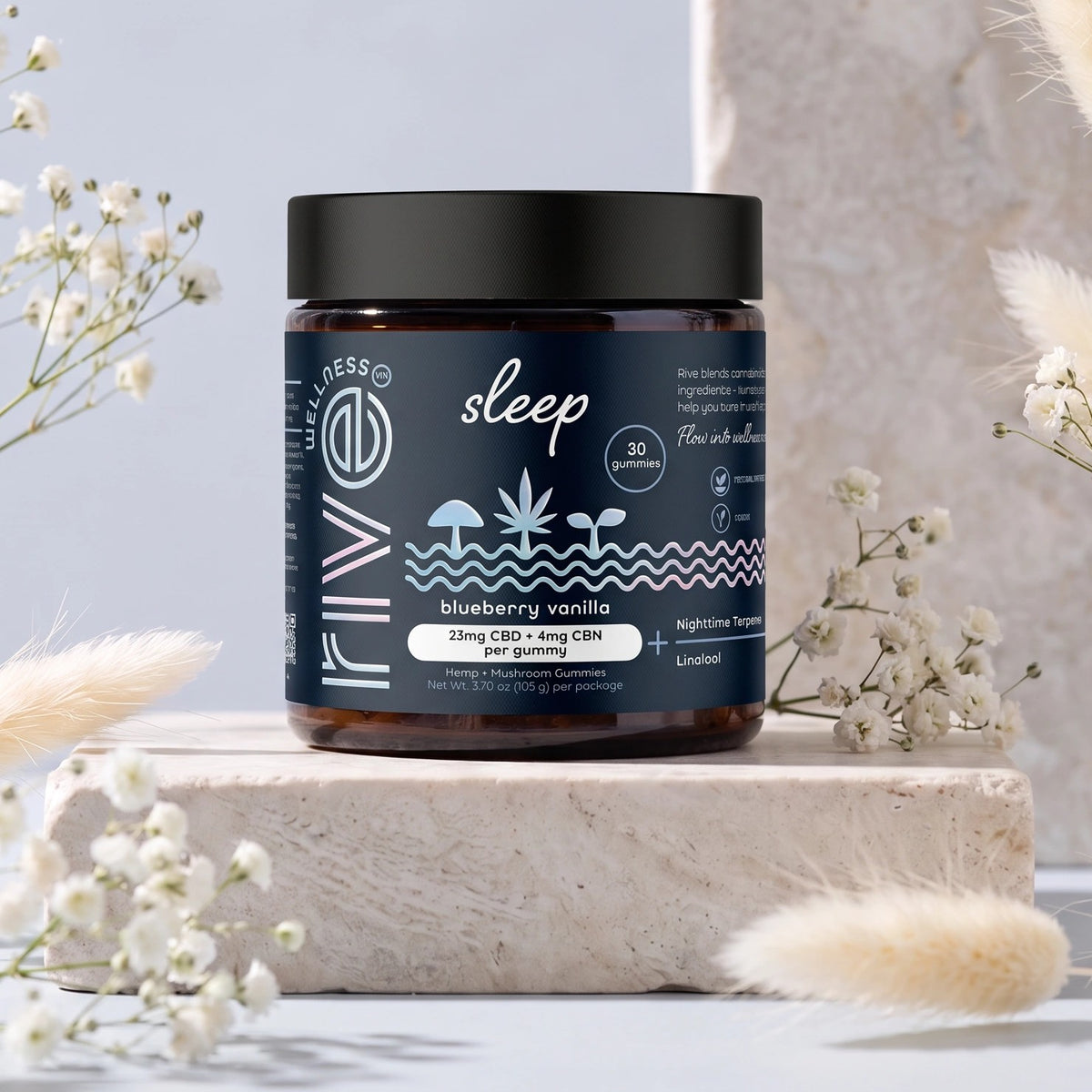 A jar of Rive Sleep blueberry vanilla gummies, 30 count, on a stone block among dried grasses and white flowers